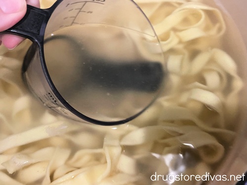 A measuring cup taking out pasta water from a pot with cooked pasta in it.