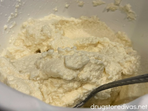 Ricotta cheese in a white bowl with a silver spoon in it.