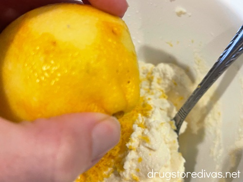 A hand squeezing a lemon into a bowl that has ricotta cheese and lemon zest in it.
