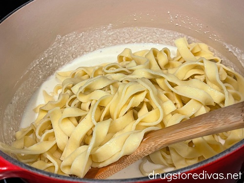Pasta in a pot with a white sauce under it and a bamboo spoon next to it.