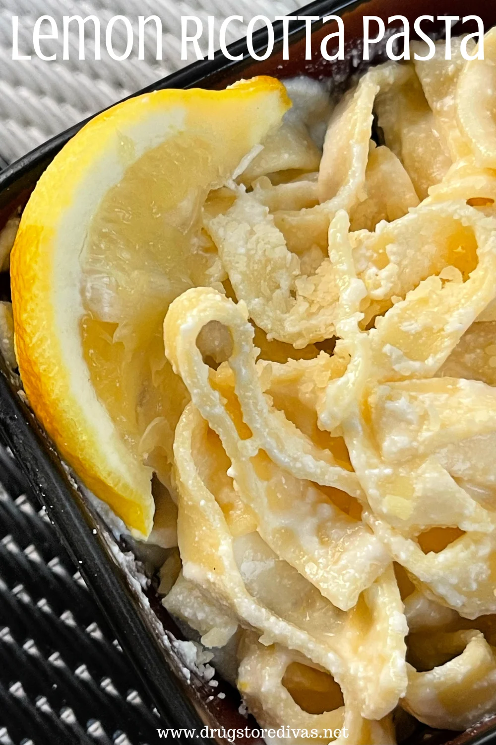 A bowl of fettuccini pasta in a cream sauce with a lemon wedge on the side of the bowl with the words "Lemon Ricotta Pasta" digitally written on top.