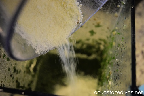 Parmesan cheese being poured into a blender with kale pesto.