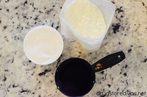 A container of yogurt, a bag of cake mix, and a cup of water on a counter.