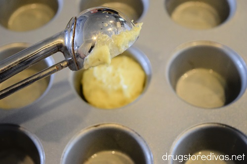 A cookie scoop putting yellow batter into a mini muffin pan.