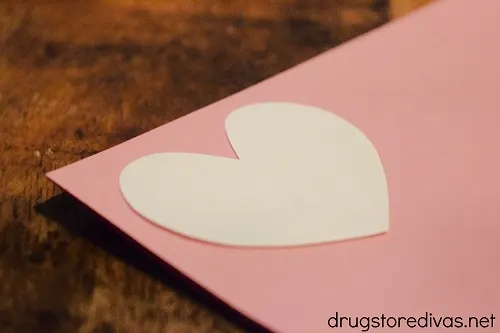 A white heart on top of a pink piece of card stock.