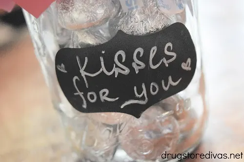 A sticker that says "kisses for you" on a mason jar filled with Hershey's Kisses.