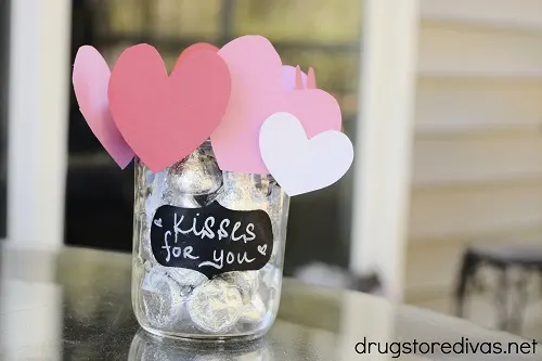A DIY "Kisses For You" Hershey's Kisses Mason Jar Gift for Valentine's Day on a table.