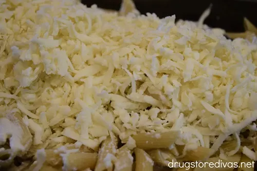 Mozzarella cheese on top of penne pasta in a baking pan.