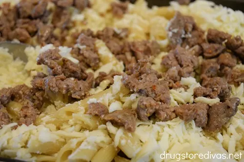 Cooked sausage and mozzarella cheese on top of penne pasta in a baking pan.
