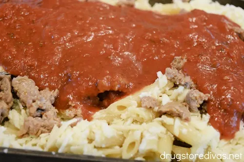 Sausage, cooked sausage, and mozzarella cheese on top of penne pasta in a baking pan.