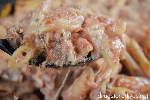 A spoonful of baked ziti with sausage above a tray of baked ziti.