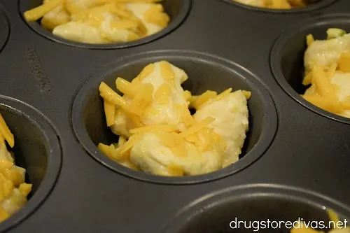 Raw biscuit dough pieces and cheese in a muffin pan.