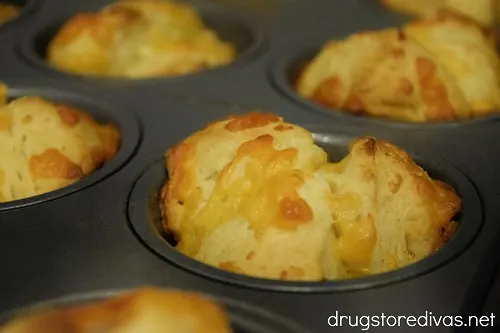 Cooked biscuit dough pieces and cheese in a muffin pan.