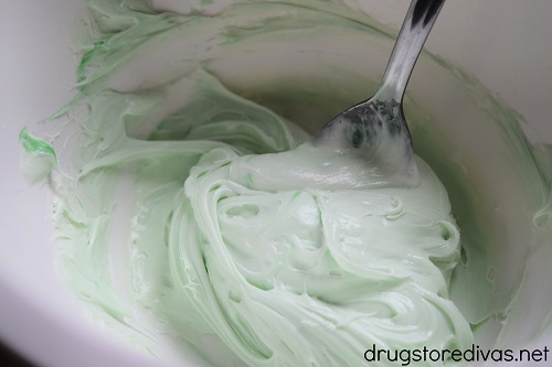 Light green frosting and a spoon in a white bowl.