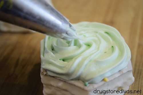 Light green frosting being piped onto a small white cake.