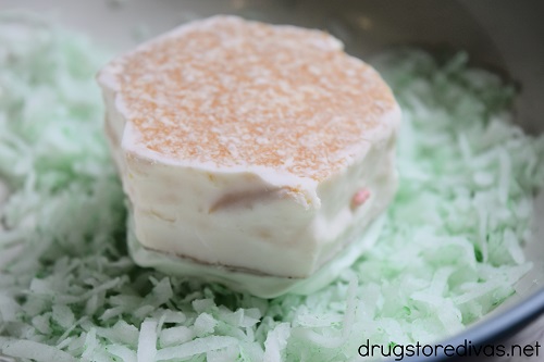 A small white cake upside down in green coconut flakes.