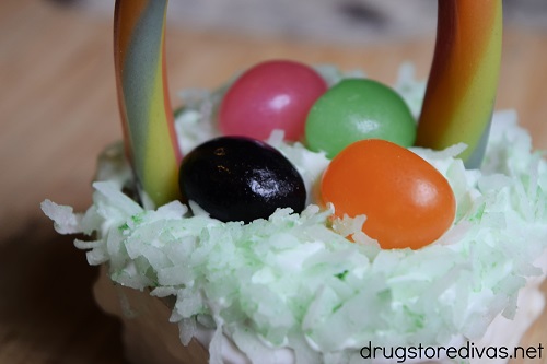 A candy rope and four jelly beans stuck into green coconut on top of a mini cake.