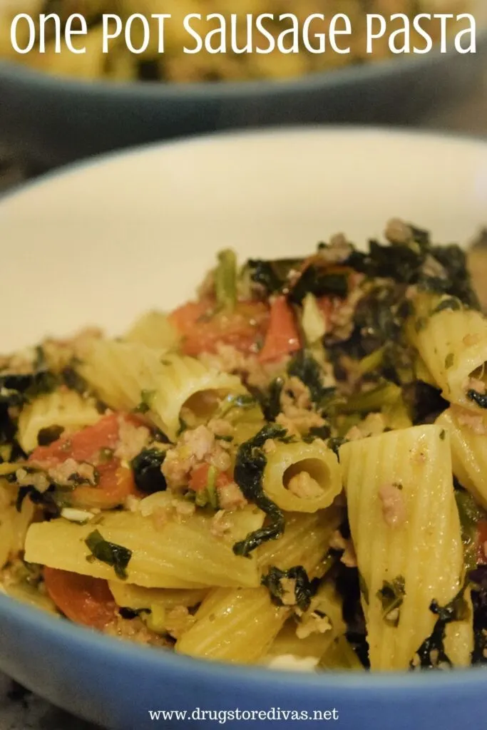 Sausage, rigatoni pasta, kale, and tomatoes in a bowl with the words "One Pot Sausage Pasta" digitally written on top.