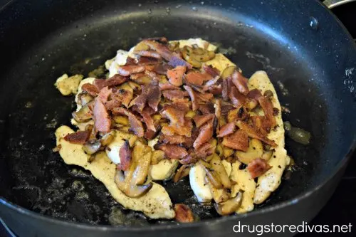 Chicken breast tenderloins, topped with bacon, in a pan.