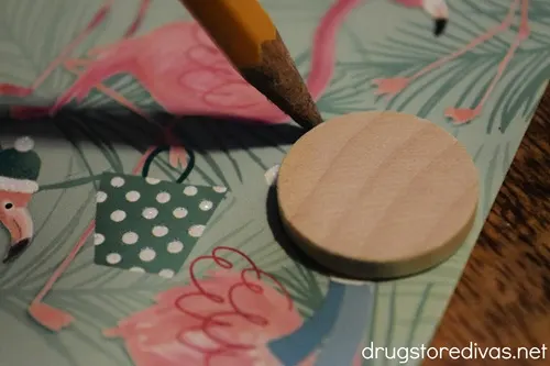 A round, wooden circle on top of a flamingo-themed Christmas card being outlined with a pencil.