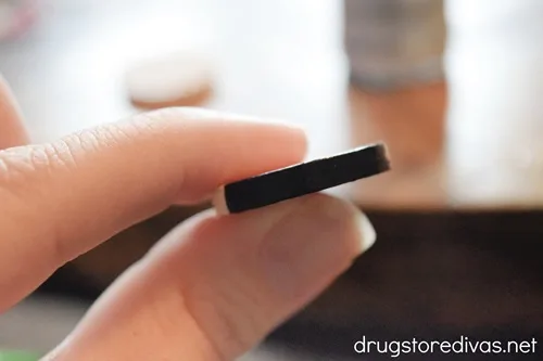 A black wooden slice between two fingers.