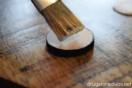 A paint brush painting a round, wooden circle.