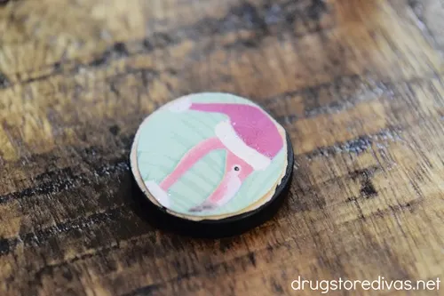 A round cutout that has a flamingo in a Christmas hat on a round, wooden slice.