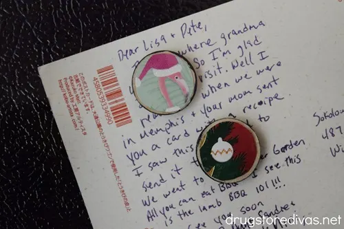 Two homemade Christmas magnets holding up a postcard that has a lot of writing on it.