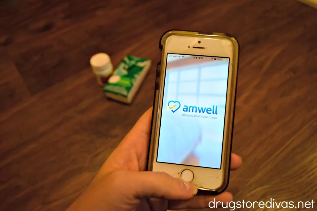 A hand holding a cell phone with medicine and tissues nearby.