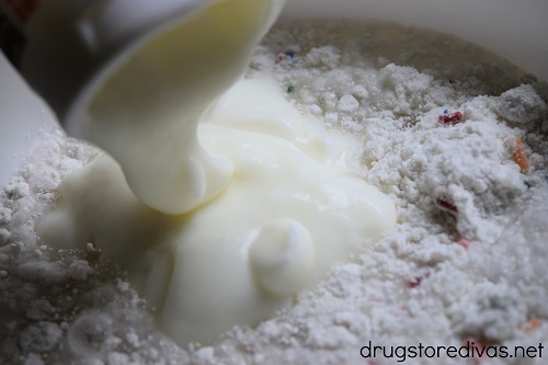 Yogurt pouring into cake mix in a bowl.