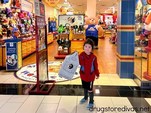 A boy holding a box in front of a Build-A-Bear Workshop.