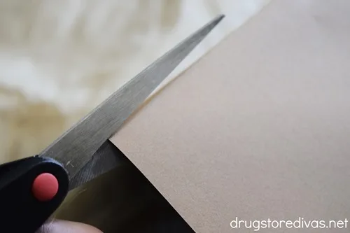Scissors cutting a piece of brown card stock.