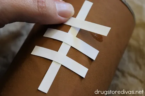 A hand sticking down white card stock that's cut to look like football laces.