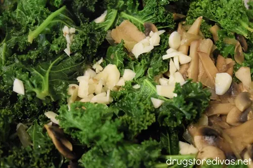 Chopped garlic, sliced mushrooms, and kale in a silver skillet.