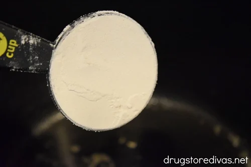 Flour in a measuring cup about to be poured into a large pot.