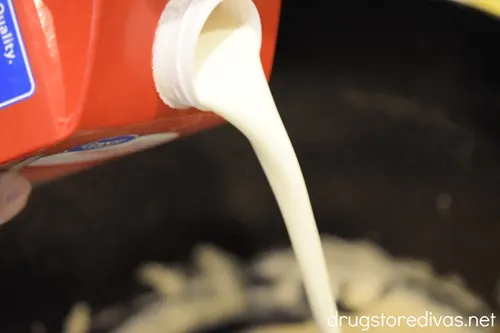 Heavy cream in a carton being poured into a large pot.