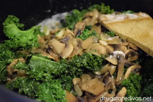 White sauce and cooked kale and sliced mushrooms in a pot.