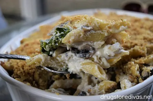 A spoon pulling some Mushroom and Kale Pasta Bake out of a casserole pan.