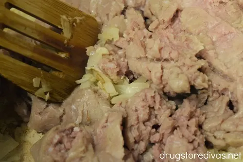 A wooden spoon breaking up ground turkey in a pot.