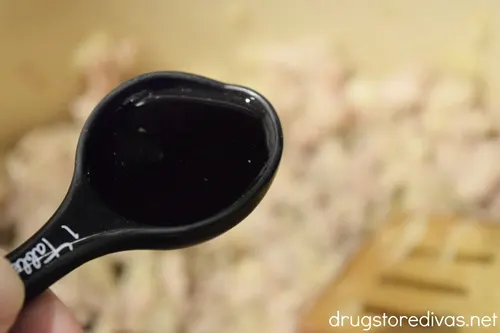 A measuring spoon with dark liquid over a pan with a wooden spoon and meat in it.