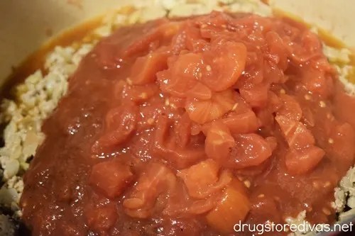 Canned tomatoes poured on top of ground meat in a Dutch oven.