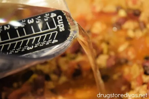 Water being poured from a measuring cup onto chili in a Dutch oven.