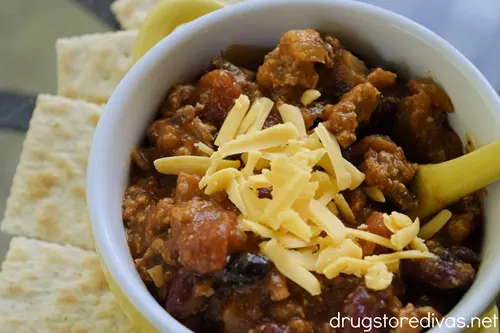 Turkey chili with yellow cheese on top in a yellow bow next to saltine crackersl.