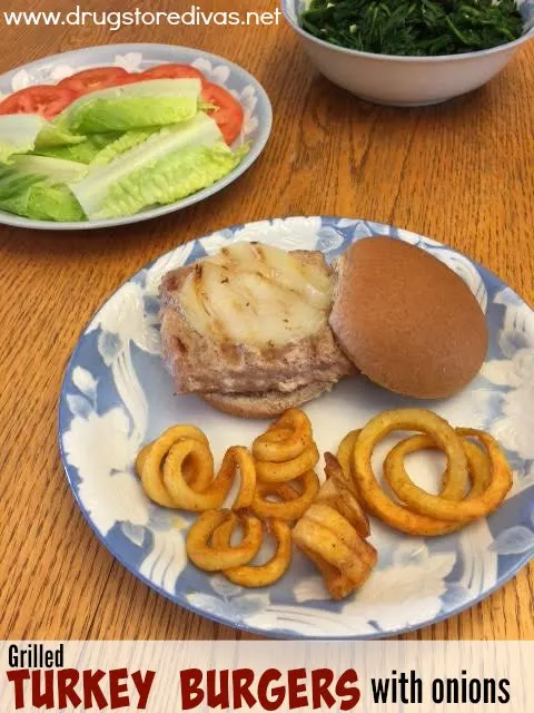 Turkey burgers with onions on a plate with curly fries and lettuce and tomato on another plate.