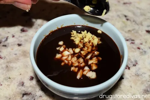 Chopped garlic being added to a dark sauce in a blue bowl.