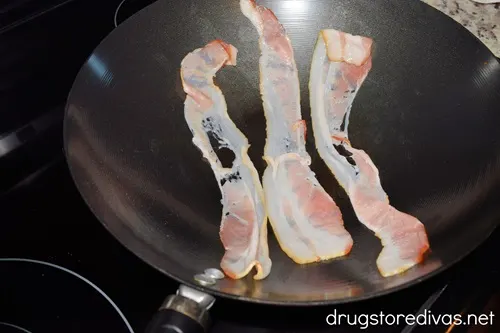Three slices of uncooked bacon in a wok.