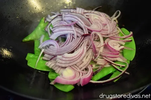 Sliced red onion and snow peas in a wok.