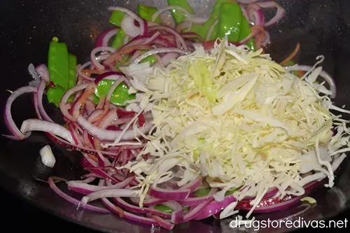 Shredded cabbage, sliced red onion, and snow peas in a wok.