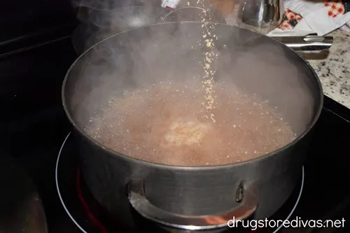 Dried seasoning being added to a large pot filled with dark broth.