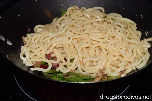 Cooked udon noodles in a wok on top of vegetables.